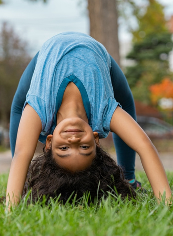 A child is doing a back bend and looking at the camera upside down. 